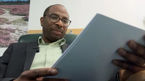 A man is looking down at a piece of paper in his hands. The man is wearing glasses. 