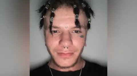 Police photograph of Thomas Holford, 24, who is accused of murdering his baby daughter. He has braided hair, facial tattoos and a nose ring.