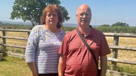 Steve Willetts A photo of Jo Kendall and Steve Willetts standing in front of a wooden fence with green fields and tress in the background.