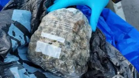 A large amount of cannabis in a clear plastic bag. The bag rests on other plastic bagging of black and blue colour.