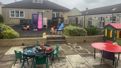 Northampton General Hospital The play area as it currently appears featuring two plastic slides, a playhouse and a table and chairs with dinosaur toys on top of it.