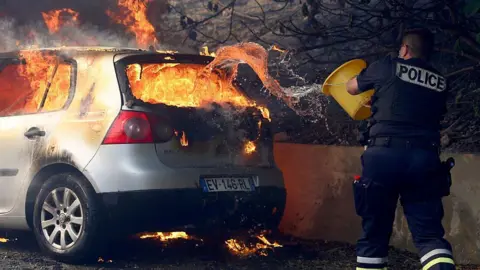 Getty Images A police officer tries to put off the fire in a car during a wildfire