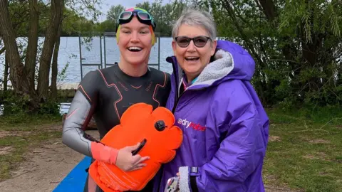 Supplied The pair near to a lake, with the daughter in a wetsuit and goggles and holding a float, and the mother in a purple dryrobe