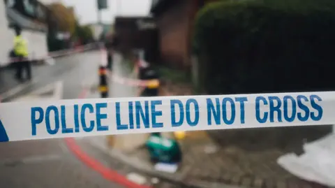 White and blue police cordon tape and the mess on the street in the background, in the place of the crime scene.