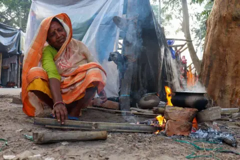 Getty Images A woman wearing an orange saree cooks food on a wood fire stove at a transit camp in India's Kolkata city in 2024.