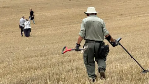 Tommy Coleman A group of metal detectorists in a field on a bright sunny day. 