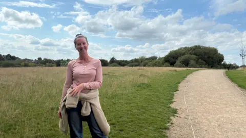 Local Democracy Reporting Service A woman in a pink top smiles to the camera whilst standing on a green field. 