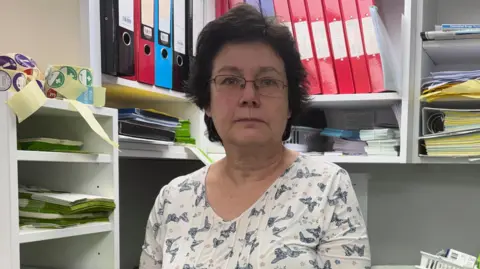 Julie Jones stands in the pharmacy surrounded by baskets of prescriptions and to her right sit several prescription forms that can't be filled