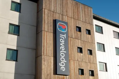 Avalon/Getty Images A Travelodge hotel with a wooden and white facade.