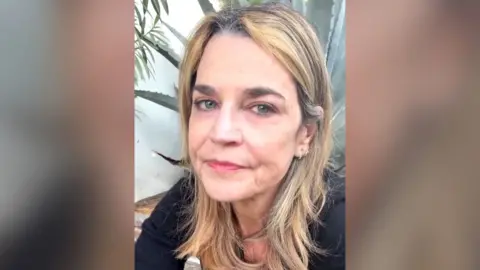 Savannah Guthrie looks into the camera as she issues a plea while sitting in front of a plant and a white wall.