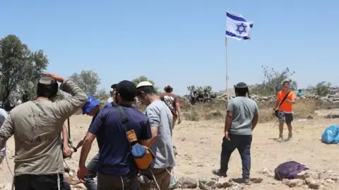 EPA A group of Israeli settlers standing around or near an Israeli flag in the occupied West Bank (file photo)