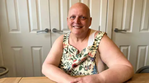 Lauren Carter/BBC Lorraine Howard, who is wearing a yellow top with flowers on and is smiling at the camera