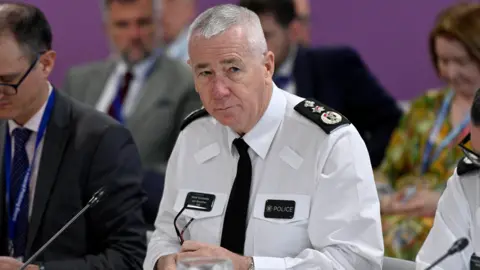 PA Media A man with white hair and white shirt with PSNI logo