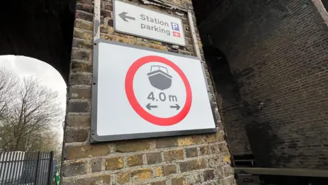 Richard Smith/BBC A sign between two of the viaduct's arches. It's a rectangular sign with a black border. The background is white and there's the shape of a boat within a red circle. Arrows within the sign suggests the arches are four metres apart