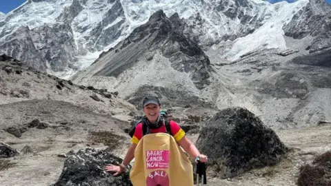 Sally Orange A woman wearing a costume stands in front of a mountain. The costume has the words "Breast Cancer Now" and "Sally" at the front.