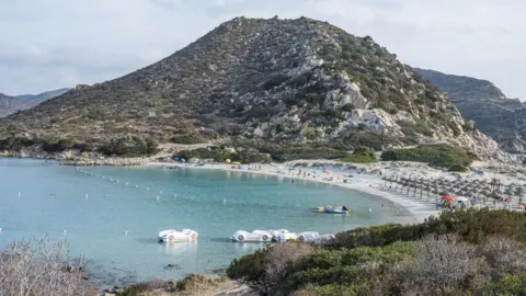 Getty Images Punta Molentis in Villasimius with white sand and turquoise water. Paddle boats can be seen in the water and umbrellas on the beachfront.