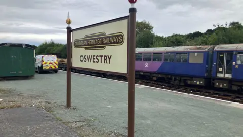A brown and beige platform sign at Oswestry station.
