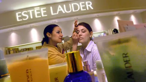 Getty Images One Estee Lauder workers applies make up on a person as they stand behind beauty products at the Estee Lauder counter