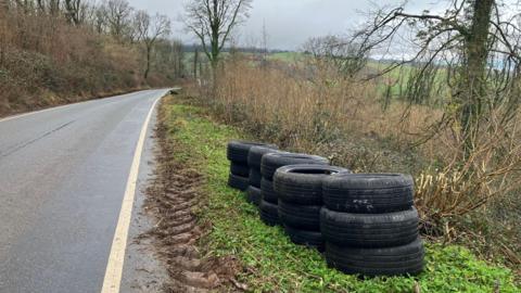 Car tyres in piles on the grass verge beside a country road on the Quantock Hills.
