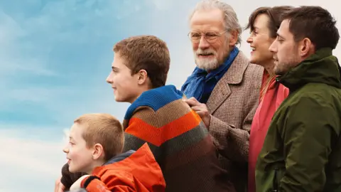 A film publicity image of two young boys, two middle-aged adults and an older gentleman. They are smiling and looking to the left.