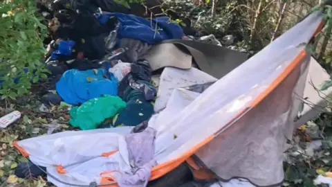 Newry LN A screen grab of footage of Fisher Park, Newry, filmed in November 2024.  Bags of rubbish and the remains of a damaged tent are discarded in piles on the ground. 