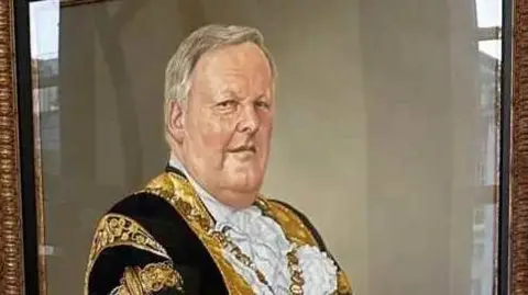 Belfast City Council Painted portrait of a man wearing a black and gold gown with a gold medal. Portrait is hung in a frame on the wall.
