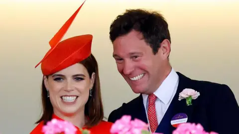 Max Mumby/Indigo/Getty Images The couple both have big smiles and are dressed in formal clothing. The princess is wearing a red hat with a large red feather on it. 