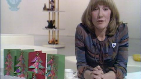 Lesley Judd leaning on a table next to her Christmas cards.