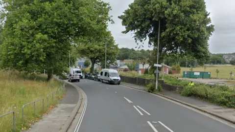 A streetview image of Kings Road. There are several cars parked along one side of the road, and a grassy patch on the other.