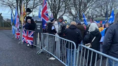 People gathered behind barrier draped with Union flags and Saltires.