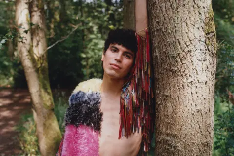 Island Records Jacob Alon leans against a tree in a lush green woodscape