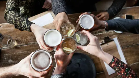 Getty Images Close up of hands raising drinks, includes beer and short drinks with ice and lemon