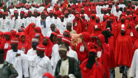 Getty Images Brides in red and grooms in white arriving at the central mosque in Kano for a mass wedding - October 2023