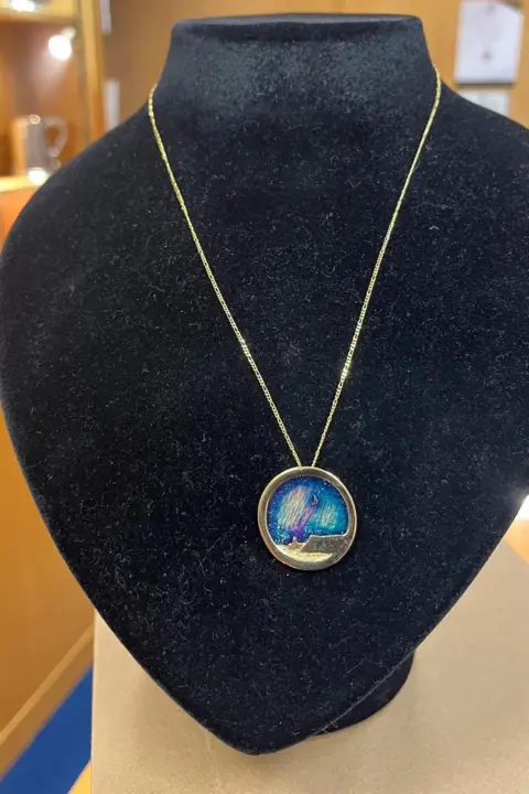 A silver pendant hanging on a display