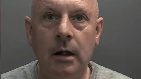 Humberside Police Custody photograph of David Rudki. He has a shaved head and is wearing a grey T-shirt