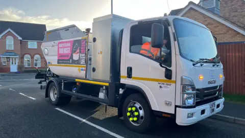 A small white bin lorry on a road in a residential area.