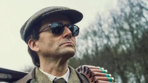 Disney+ David Tennant in cap and sunglasses, like the "resolutely ambitious and selfish" Lord Tony Baddingham