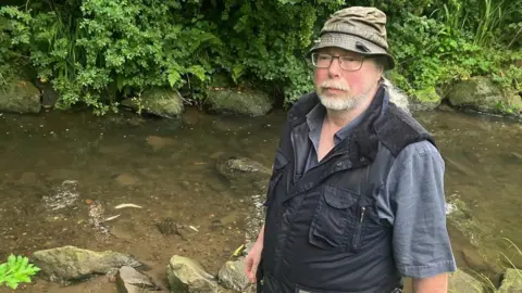 Man standing next to river with dead fish.