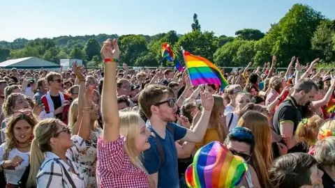 A crowd raising their hands in the air and waving rainbow Pride flags during a Pride event in Durham