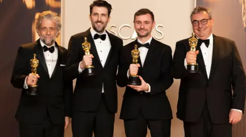 Getty Images Paul Lambert, Stephen James, Rhys Salcome, Gerd Nefzer collecting their award at the Oscars ceremony. They are wearing black tuxedos.
