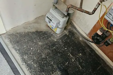David O'Reilly A picture of a speckled black and grey floor with an electric machine in the far corner. 