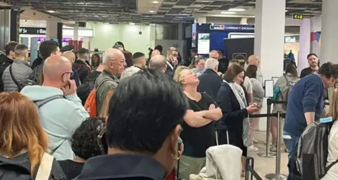 Lisa Ruston A queue of passengers waiting to get through to the airport's security gates - their expressions suggest they have been waiting some time.