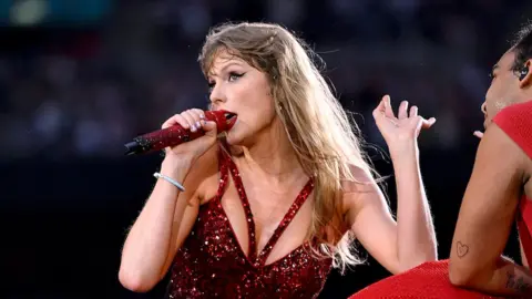 Getty Images Taylor Swift performing in a red top with matching microphone.