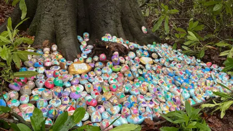 A huge collection of "fairy rocks" painted in bright colours at the bottom of a tree.