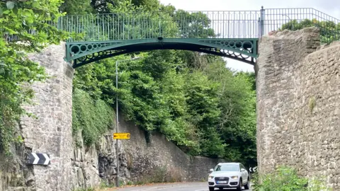 The footbridge newly installed over a road, with a car driving underneath