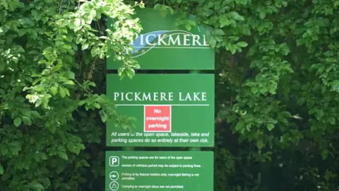 Green sign at the entrance to Pick Mere warning 'all users of the open space, lakeside, and lake do so entirely at their own risk'.