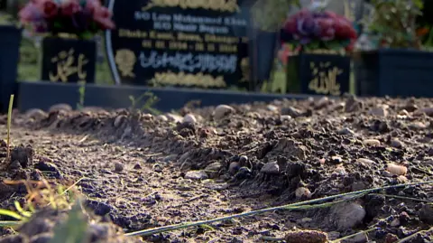 A photo of mud in the ground and in the background you can see a gravestone.