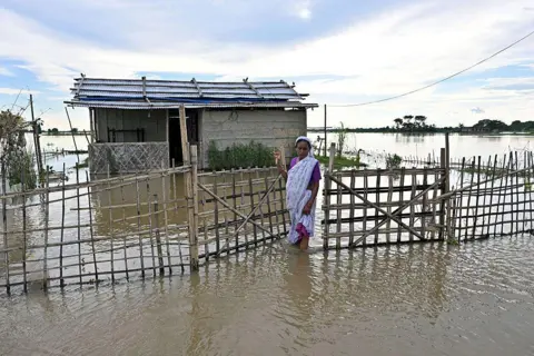 A woman wades through floodwaters outside her inundated house at a village in Assam's Sivasagar 
