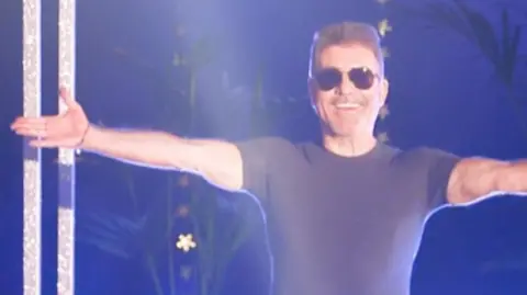 Simon Cowell with his arms outstretched