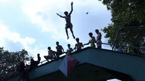 A person jumps off a bridge into the Canal Saint-Martin as public swimming having been allowed earlier on part of it due to rising of temperatures